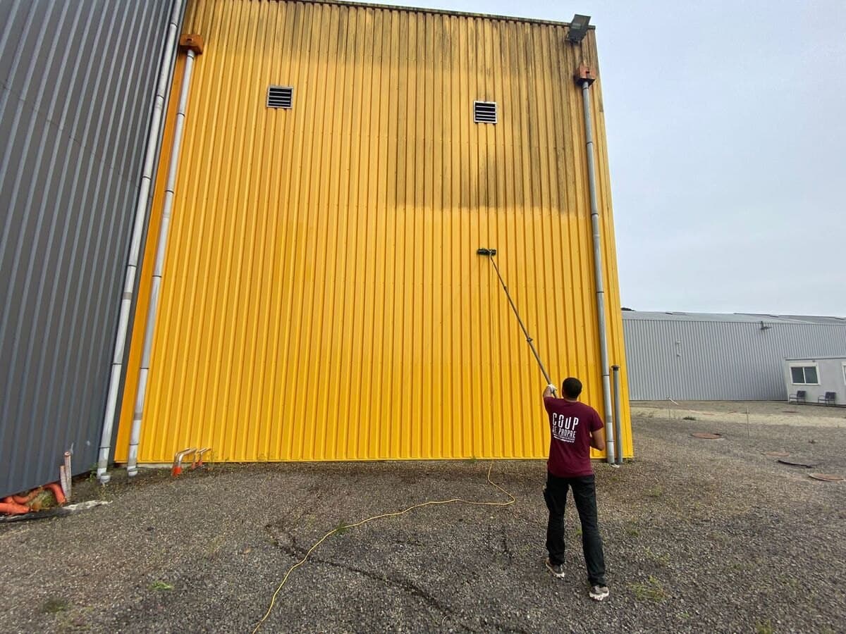 Nettoyage d'un bardage métallique jaune de bâtiment industriel à la brosse télescopique